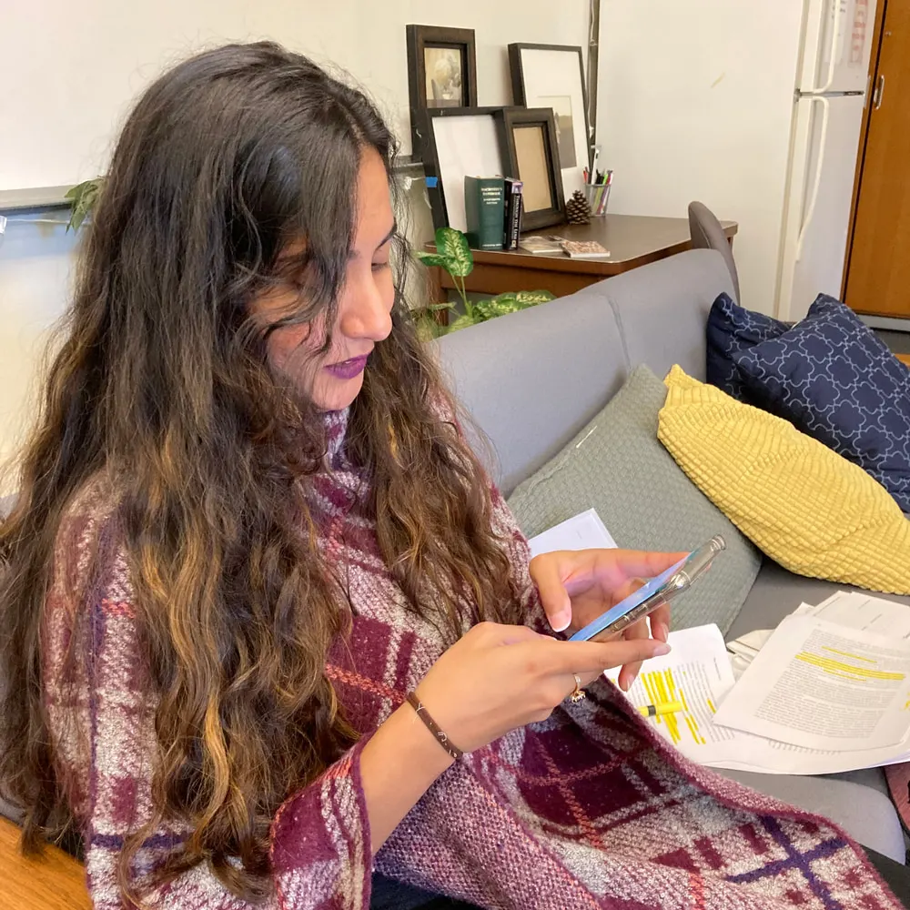 A user testing session: a participant sitting on a sofa working through the Hodo prototype on her phone, with printed and highlighted test notes beside her