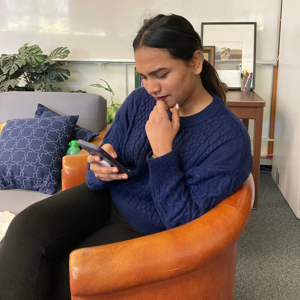 A second user testing session: a participant in an armchair reading a Hodo screen on her phone with her hand at her chin